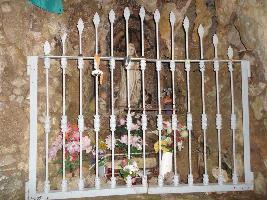 Image of the Virgin behind the white railing, surrounded by flowers, in the Cova de la Verge de Falgars