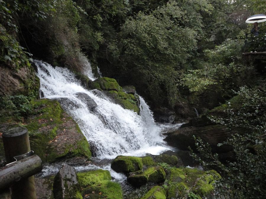 Cascade des Fonts del Llobregat entre des rochers moussus, vue depuis le garde-corps en bois du sentier