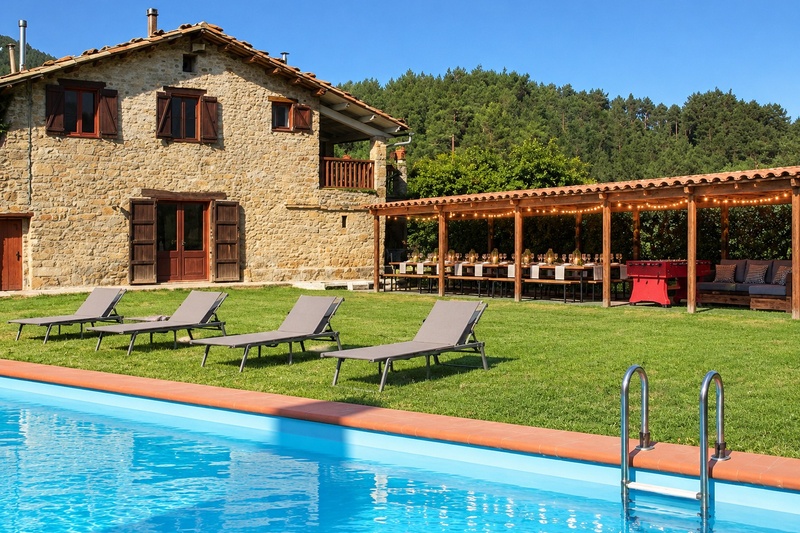 Espacio exterior cubierto con mesa grande, zona chill-out y piscina en la Masía El Pati en Borredà